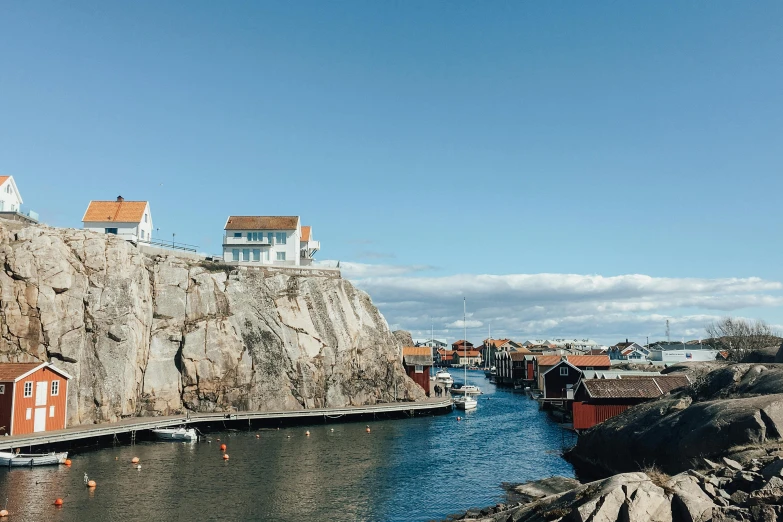 a group of houses sitting on top of a cliff next to a body of water, by Jesper Knudsen, pexels contest winner, alvar aalto, harbour, blue sky, thumbnail