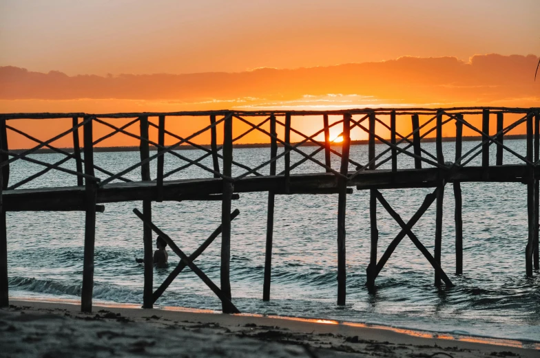 a pier stretches out into the ocean at sunset, by Niko Henrichon, pexels contest winner, wooden structures, australian beach, vine bridge silhouette over lake, sunset lighting 8k