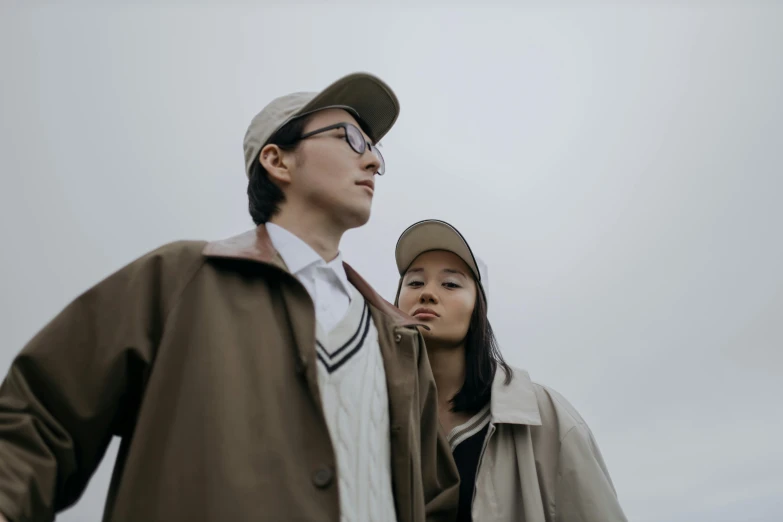 a man and a woman standing next to each other, trending on pexels, light brown coat, asian human, gray sky, avatar image
