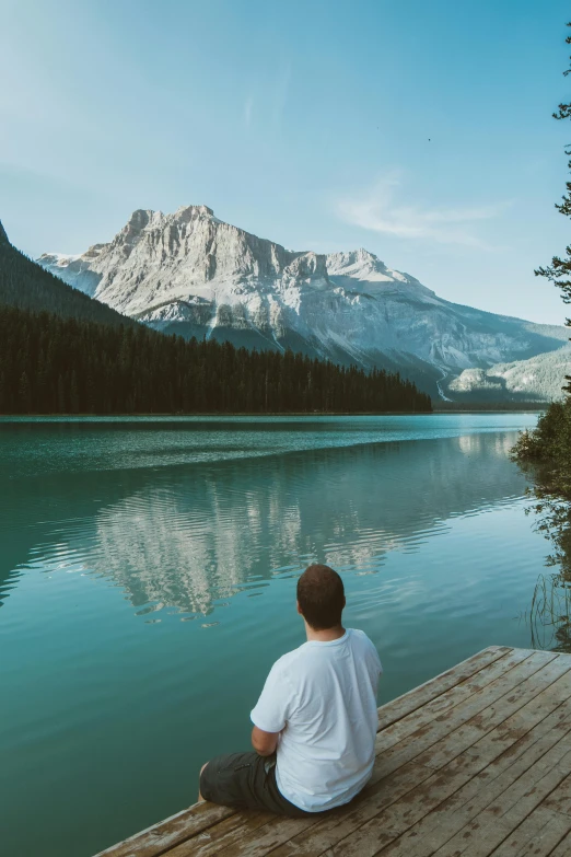 a man sitting on a dock next to a body of water, pexels contest winner, banff national park, blonde man, distant thoughtful look, teal landscape