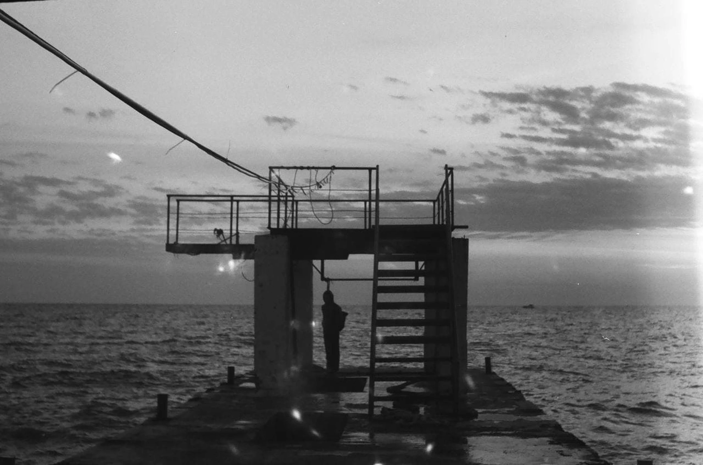 a man standing on top of a pier next to the ocean, by Maurycy Gottlieb, black sea, boat with lamp, cinema still, f / 2 0