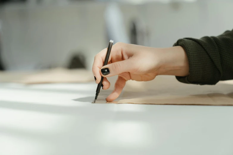 a person holding a pen and writing on a piece of paper, trending on pexels, visual art, traditional animation, looking from shoulder, modelling, on a table