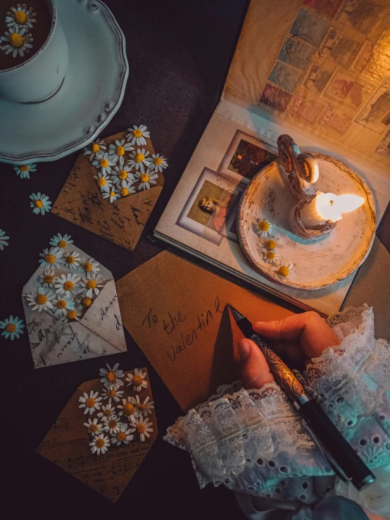 a person holding a lit candle on top of a table, inspired by Elsa Bleda, pexels contest winner, mail art, brown flowers, thumbnail, cinematic outfit photo, writing a letter