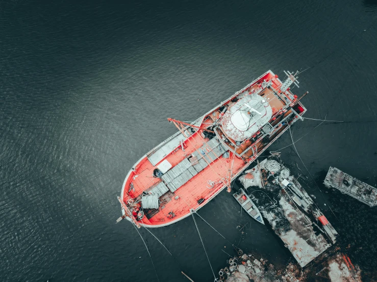 a red boat sitting on top of a body of water, by Adam Marczyński, pexels contest winner, auto-destructive art, helicopter view, shipyard, victorian fire ship, grey