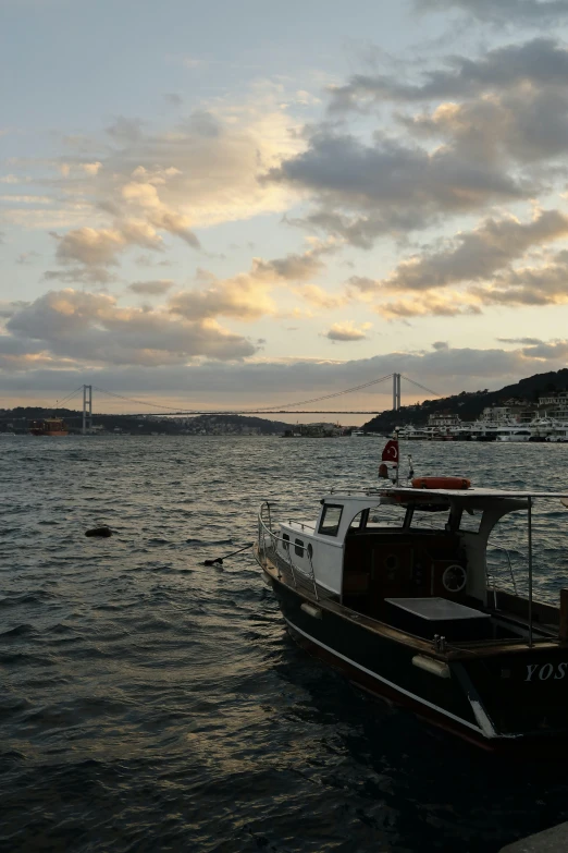 a boat that is sitting in the water, inspired by Nadim Karam, hurufiyya, dramatic lighting - n 9, istanbul, ((sunset)), connected with hanging bridge!!