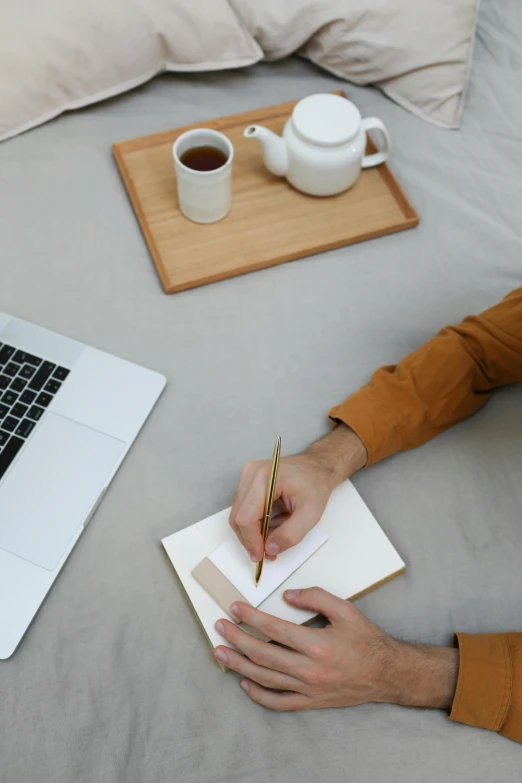 a person writing on a piece of paper in front of a laptop, next to a cup, curated collections, avatar image