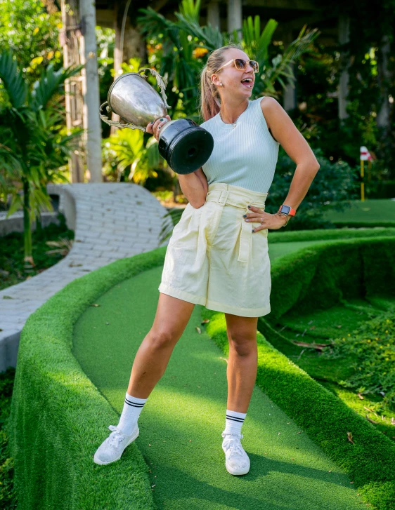 a woman standing on a miniature golf course holding a trophy, a portrait, pexels contest winner, happening, white skirt and barechest, adriana chechik, 🤬 🤮 💕 🎀, thumbnail