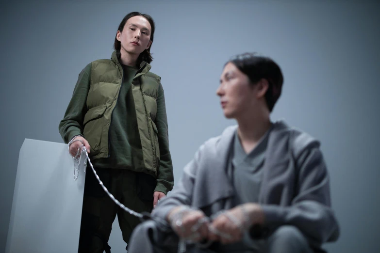 a couple of men standing next to each other, inspired by Fei Danxu, unsplash, hyperrealism, hito steyerl, with prison clothing, protagonist in foreground, sitting down