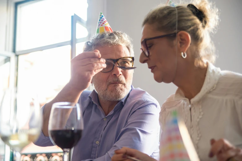 a man putting a party hat on a woman's head, pexels contest winner, figuration libre, wearing square glasses, at a birthday party, middle - age, themed after wine