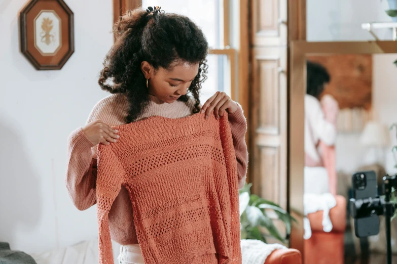 a woman standing in a living room holding a sweater, pexels contest winner, happening, pink and orange, prompt young woman, people shopping, curly haired