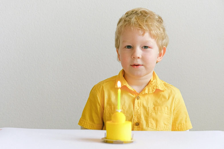 a young boy sitting at a table with a candle in front of him, pexels, king in yellow, on a white table, birthday, a blond