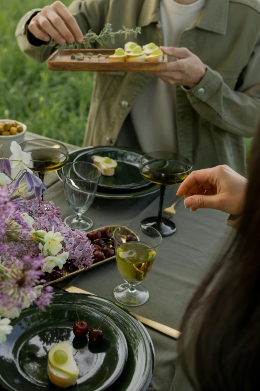 a group of people sitting around a table with plates of food, in the garden, olive oil, violet, curated collections