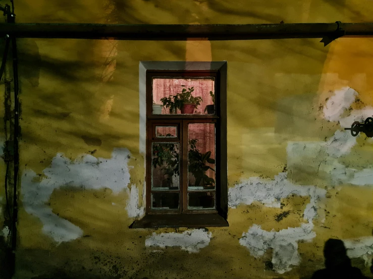 a person standing in front of a building with a window, a painting, inspired by Elsa Bleda, pexels contest winner, renaissance, faded red and yelow, open window at night, ukraine. photography, before a stucco wall