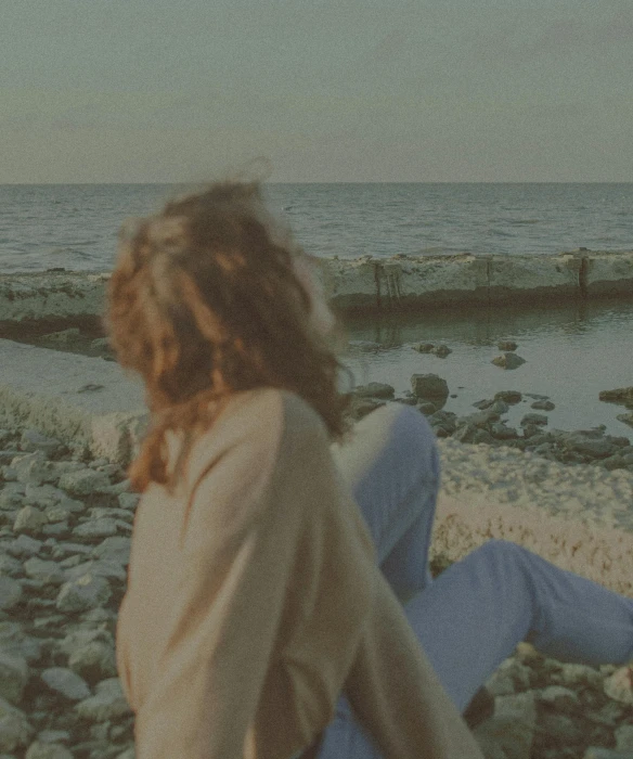 a woman sitting on a rocky beach next to the ocean, inspired by Elsa Bleda, happening, vintage muted colors, concert, loosely cropped, chillhop