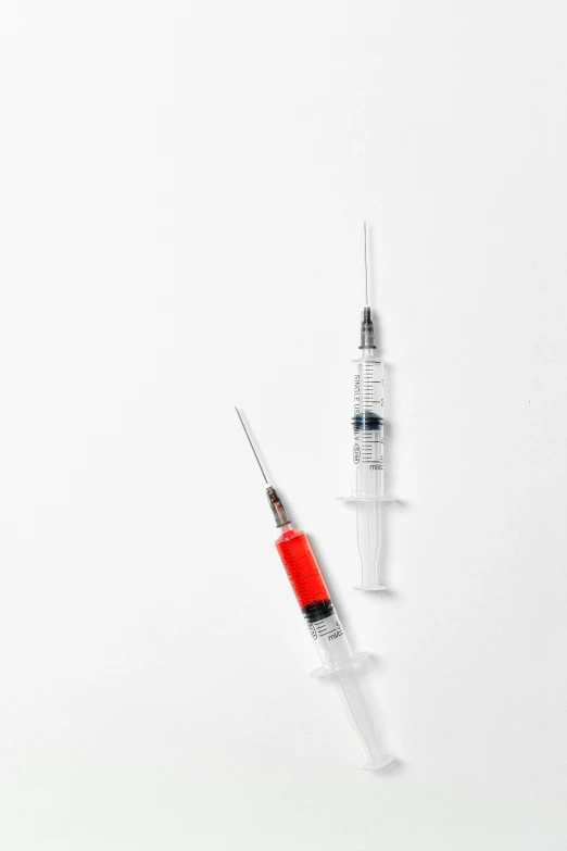 a syll and a syll on a white surface, holding a syringe, vermillion, product shot, technical