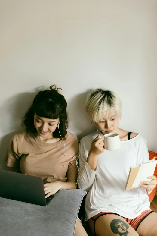 a couple of women sitting on top of a bed next to each other, trending on pexels, happening, using a macbook, small hipster coffee shop, plain background, studious