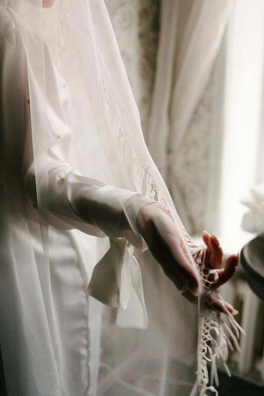 a close up of a person in a wedding dress, robe, touching her clothes, veiled, white ribbon