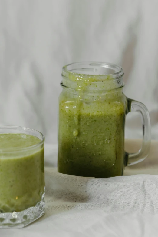 a glass of green smoothie next to a jar of green smoothie, by Alejandro Obregón, grey, low quality photo, ebay listing thumbnail, 0