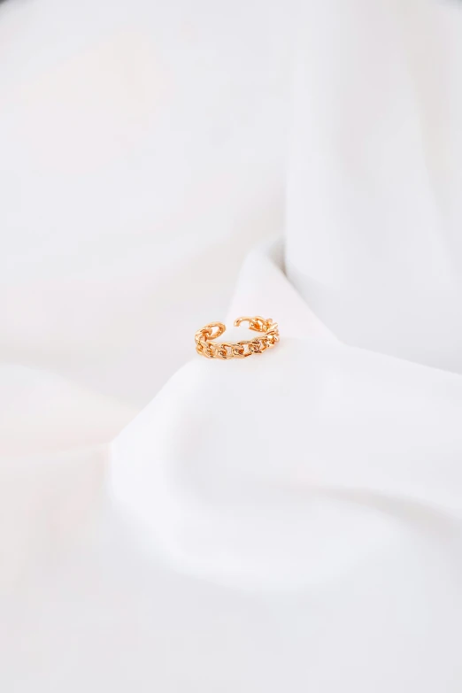 a gold ring sitting on top of a white shirt, trending on pexels, in front of white back drop, chainmail, jovana rikalo, detailed product image