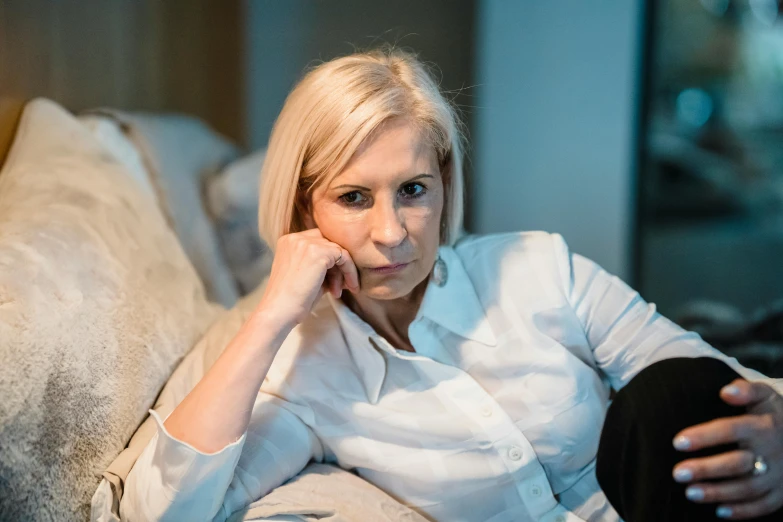 a woman in a white shirt sitting on a couch, inspired by Joanna Carrington, pexels, realism, sad look, relaxed dwarf with white hair, aged 4 0, tinnitus