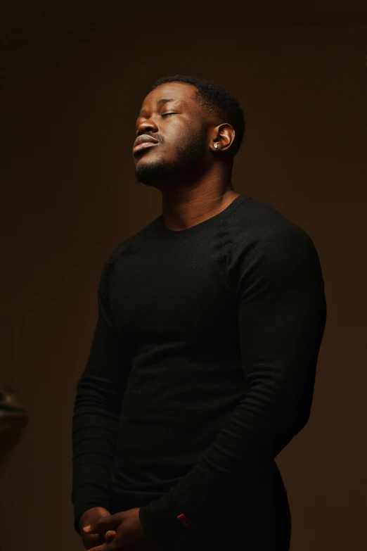 a man in a black shirt standing in a dark room, an album cover, pexels contest winner, godwin akpan, looking off to the side, profile image, he is wearing a brown sweater