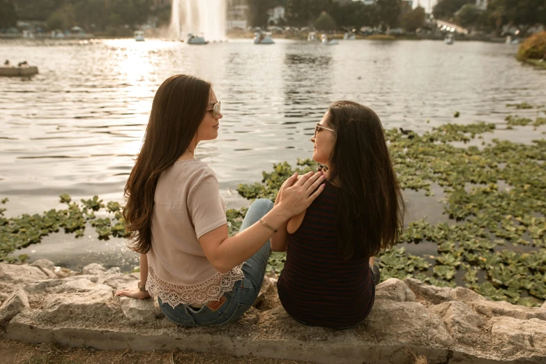 two women sitting next to each other near a lake, pexels contest winner, hurufiyya, avatar image, brunettes, lesbian embrace, in a city park