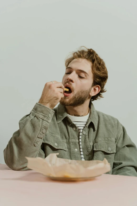 a man sitting at a table eating food, a colorized photo, trending on pexels, plain background, charlie cox, wearing jacket, about to consume you