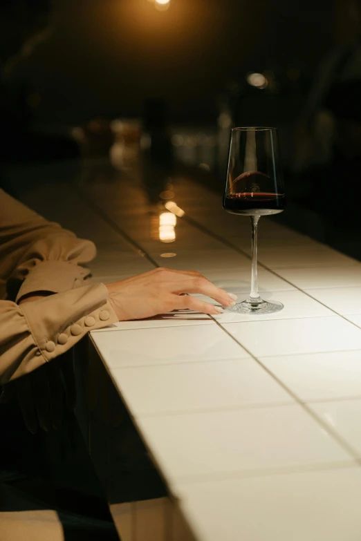 a person sitting at a table with a glass of wine, inspired by Nan Goldin, unsplash, hands on counter, mysterious ambient lighting, slightly minimal, unwind!