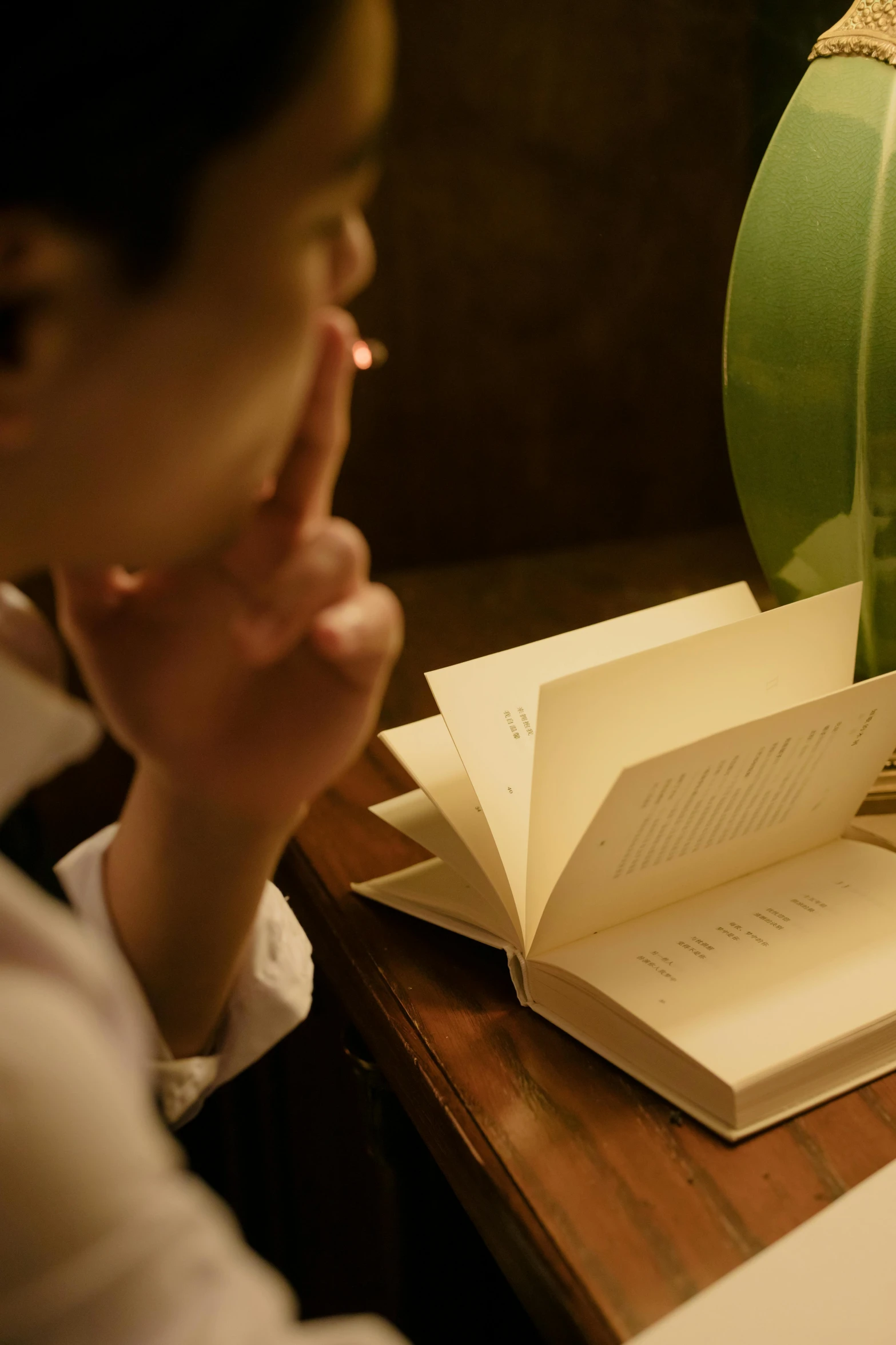 a woman sitting at a table reading a book, inspired by Clarice Beckett, unsplash, private press, hand over mouth, illuminated, ignant, vintage inspired