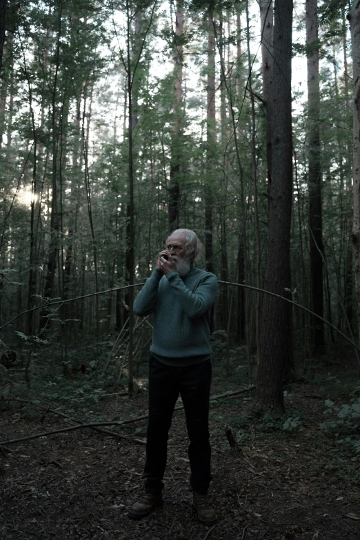 a man standing in the middle of a forest talking on a cell phone, filmstill, old man, lynn skordal, ((forest))