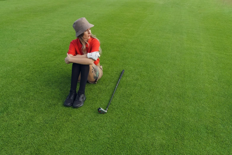 a woman kneeling on top of a green field next to a golf ball, turf roof, sitting down casually, clubs, fake grass