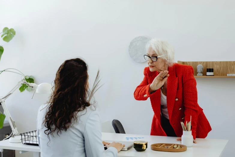 a woman talking to a woman sitting at a desk, by Emma Andijewska, pexels contest winner, local conspirologist, in white room, profile image, an old lady with red skin