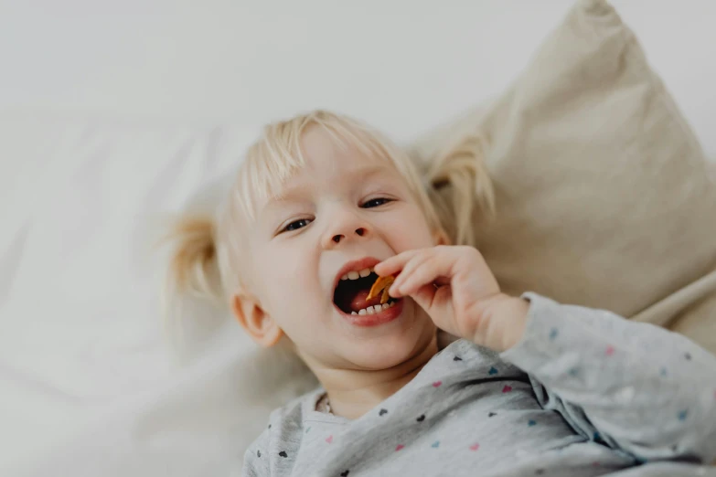 a little girl laying on a bed brushing her teeth, by Emma Andijewska, pexels contest winner, antipodeans, having a snack, cinnamon, jajaboonords flipjimtots, full product shot