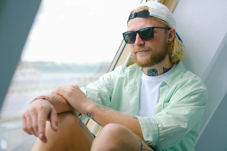 a man with a beard sitting next to a window, sea - green and white clothes, wearing oakley sunglasses, lachlan bailey, avatar image