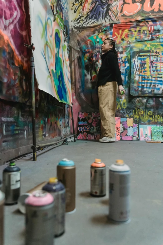 a man standing in front of a wall covered in graffiti, graffiti art, stands at her easel, spray paint, profile image