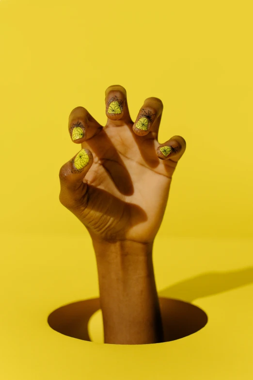 a person's hand reaching out of a hole, an album cover, inspired by Ras Akyem, trending on pexels, nail art, black. yellow, patterned, ad image