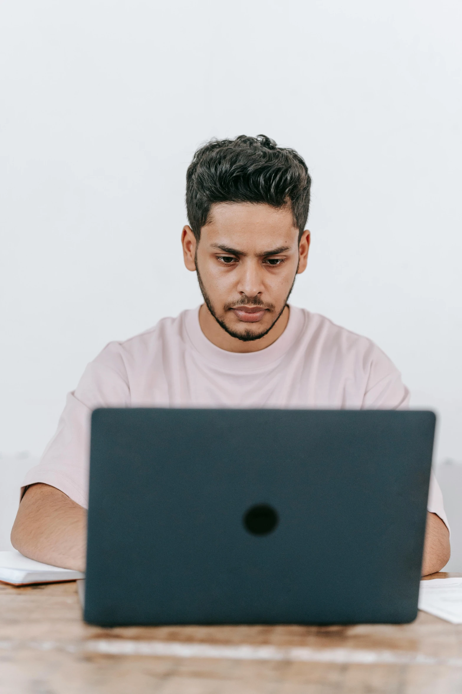 a man sitting at a table with a laptop, trending on pexels, looking serious, post graduate, middle eastern, non-binary