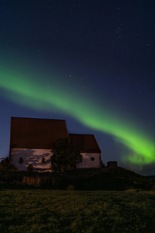 a house sitting on top of a lush green field, by Roar Kjernstad, light show, church, rustic, aurora