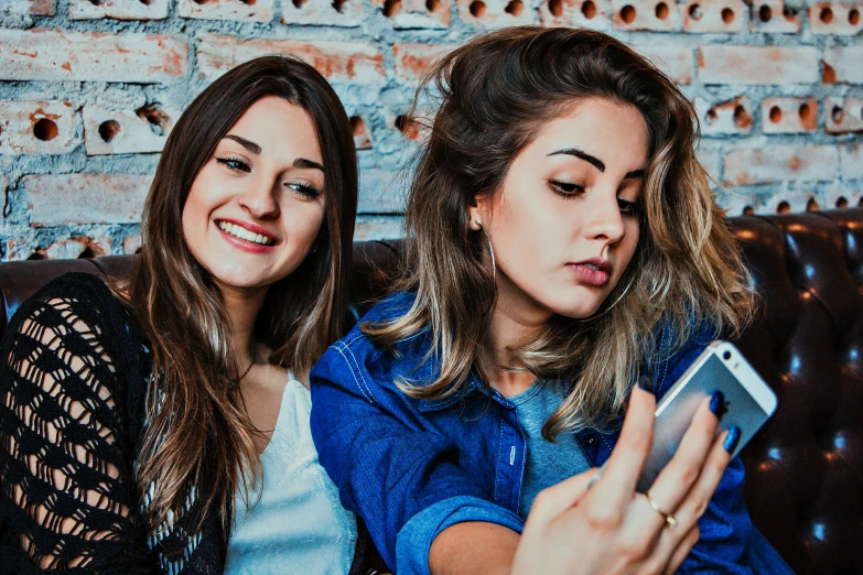 two women sitting on a couch looking at a cell phone, trending on pexels, in love selfie, one blonde and one brunette, teenage, with a long