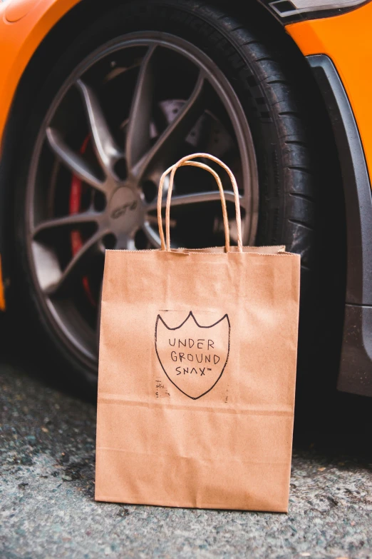 an orange sports car parked next to a brown paper bag, an album cover, unsplash, underground party, logo for lunch delivery, napa, supercar