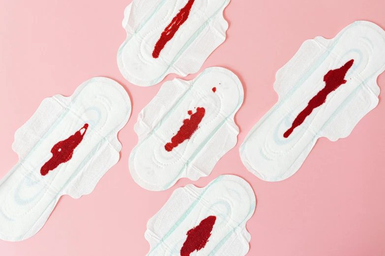 a group of disposable sanitary pads on a pink surface, inspired by Louise Bourgeois, auto-destructive art, dripping blood, detailed product image, medium level shot, close-up product photo