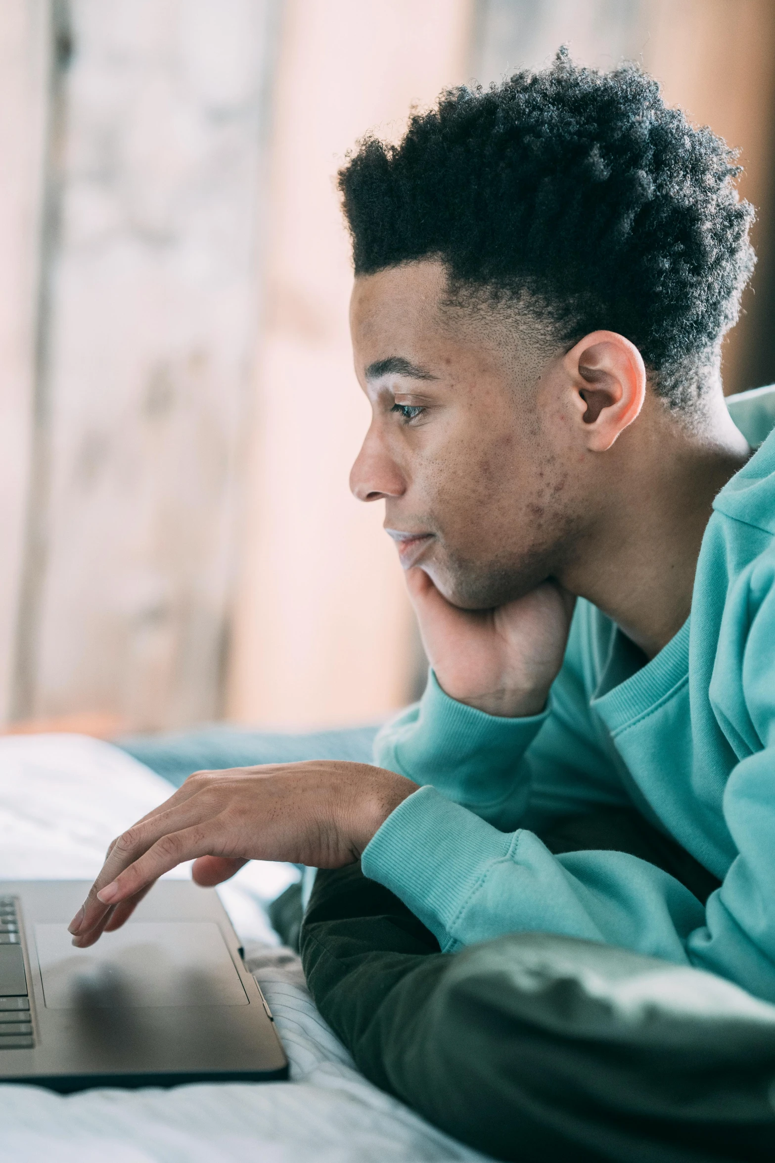 a man laying on a bed using a laptop, trending on pexels, renaissance, black teenage boy, teal color graded, looking serious, bending down slightly