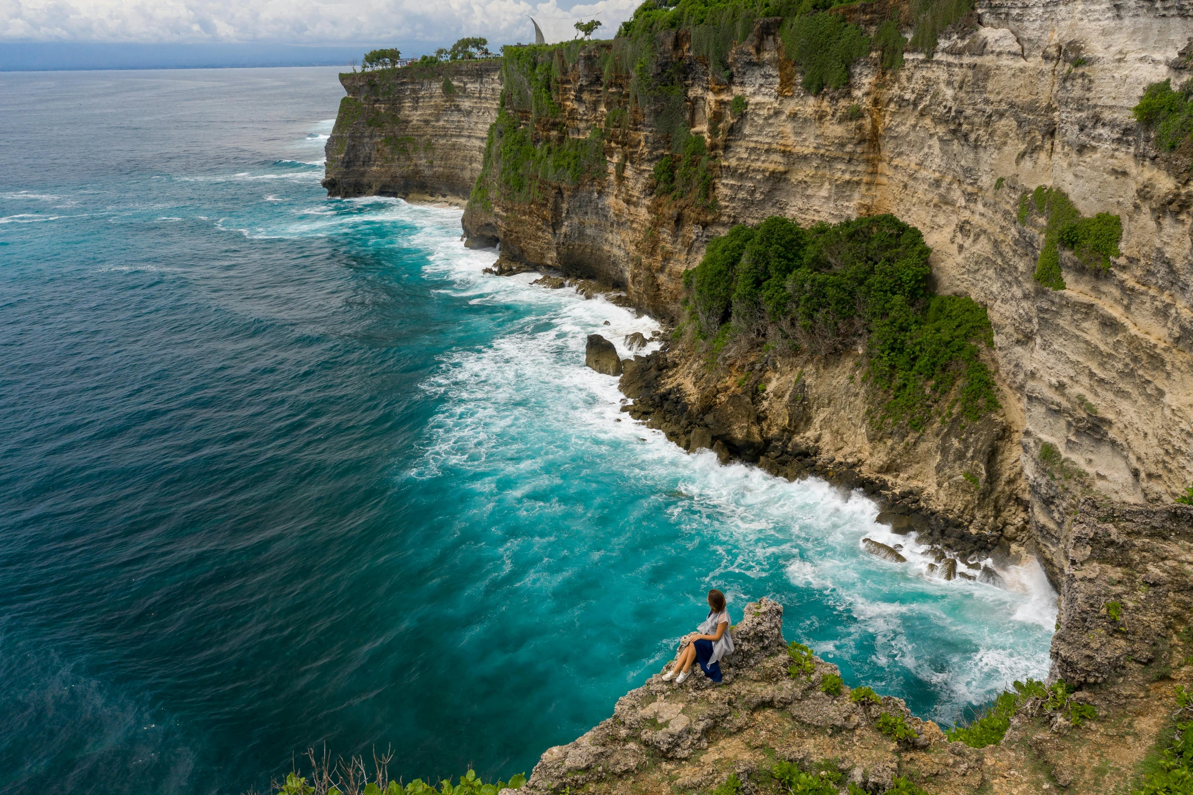 a man sitting on the edge of a cliff overlooking the ocean, bali, avatar image