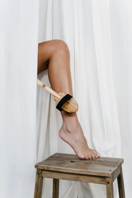 a woman sitting on top of a wooden stool, dry brushing, shows a leg, spoon placed, slightly minimal