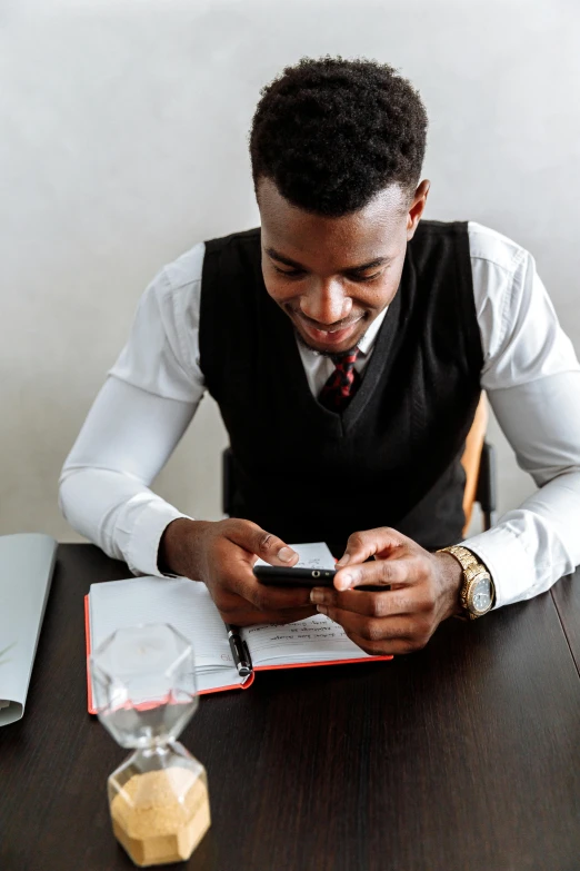 a man sitting at a table looking at his cell phone, pexels contest winner, happening, wearing a vest and a tie, man is with black skin, studious, saving the day again