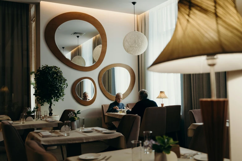 a couple of people sitting at a table in a restaurant, by Emma Andijewska, pexels contest winner, art nouveau, round mirror on the wall, john pawson, thumbnail, highly symmetrical