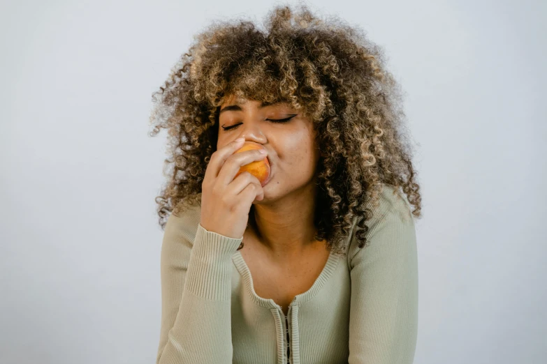 a woman with curly hair eating an orange, trending on pexels, manuka, with closed eyes, slightly pixelated, eating garlic bread