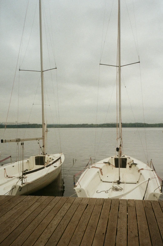 a couple of boats sitting on top of a wooden dock, very poor quality of photography, washington dc, sailboat, grey sky