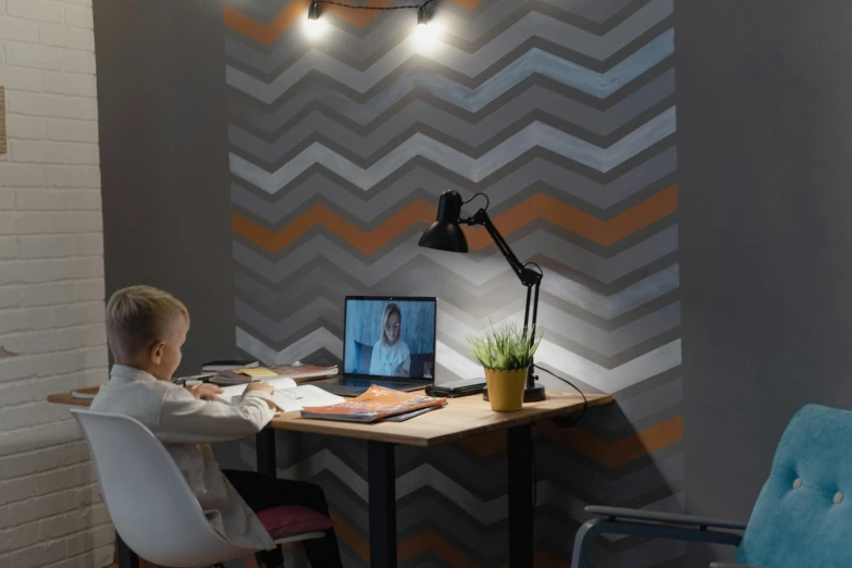 a young boy sitting at a desk in front of a laptop computer, inspired by Alexander Roslin, trending on reddit, light and space, rgb wall light, zig zag, small and cosy student bedroom, wallpaperflare