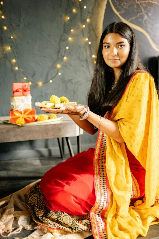 a woman sitting on the floor holding a plate of food, wearing festive clothing, sharandula, profile image, sweets